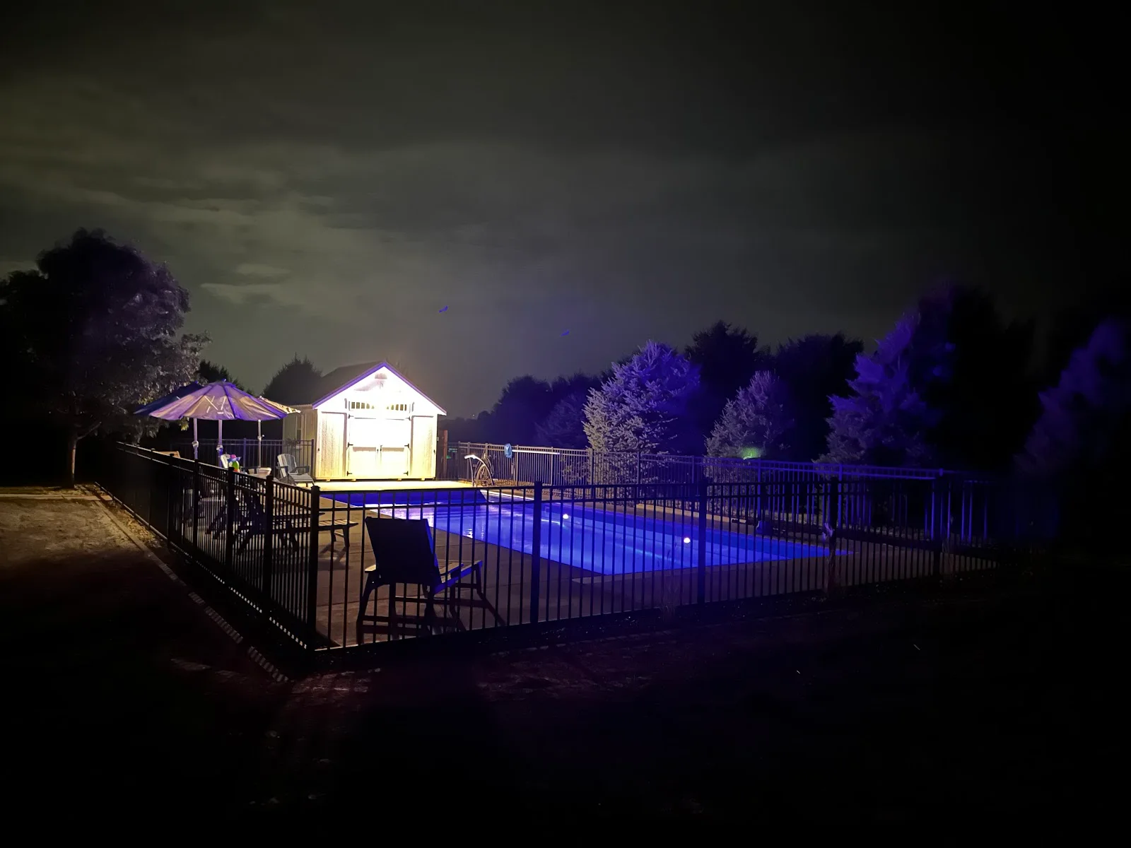 Pool lit blue at night beside a lit outbuilding, posted by homeowner Julia